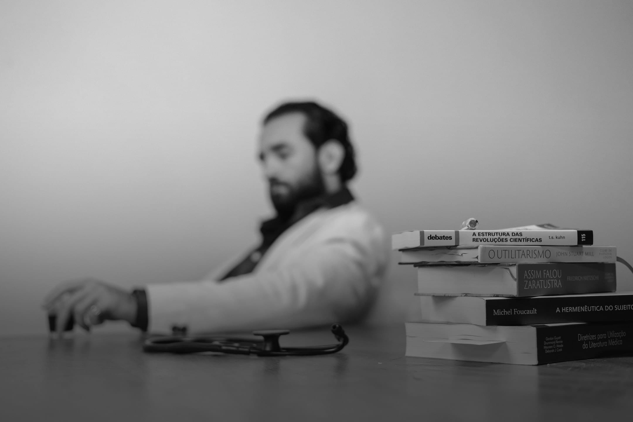 Dr. Eric Pascher à mesa, em preto e branco, com uma pilha de livros à frente